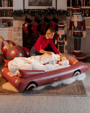 Woman with child on a red inflatable car in a festive living room with Christmas stockings and decorations.